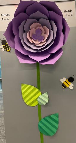 Paper flower with stem and leaves with bees, attached to the side of a bookshelf.