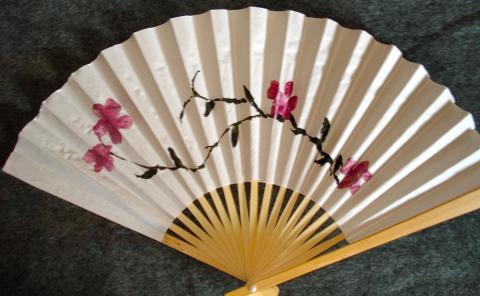 A handheld fan with watercolor flowers and branches painted on.