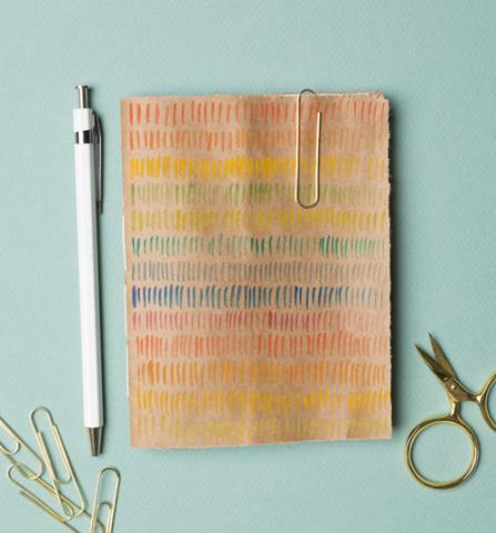 A handmade journal with rainbow lines drawn on and stationary spread around it.